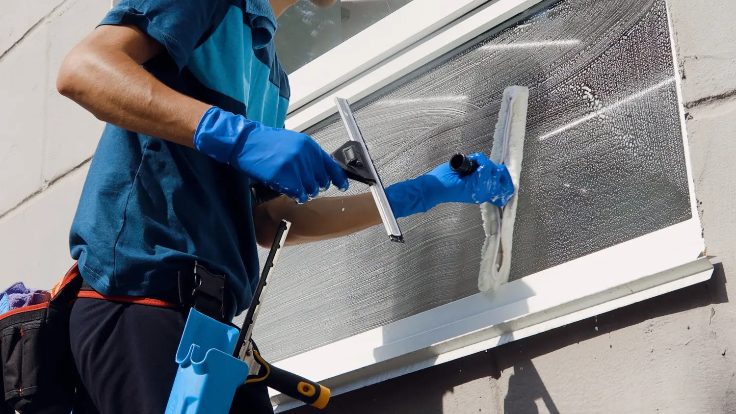 Männliche Reinigungskraft in Latzhose reinigt die Fenster und Schaufenster eines Geschäfts mit Spezialgeräten